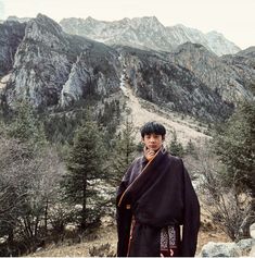 a man standing on top of a mountain with a scarf around his neck and mountains in the background