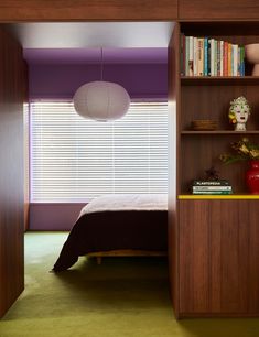 a bed sitting under a window next to a book shelf