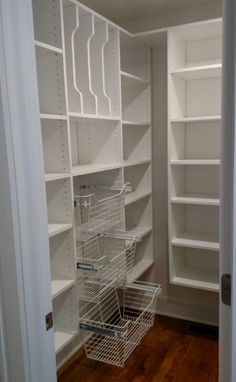 an empty walk - in closet with white shelves and baskets on the floor next to it