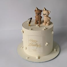 two teddy bears sitting on top of a white cake with frosting and gold decorations