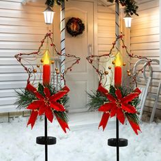 two lighted candles in front of a house decorated for christmas