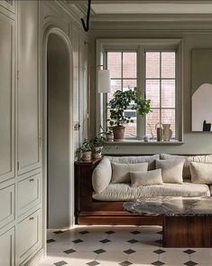 a living room filled with furniture next to a window covered in plants and potted plants