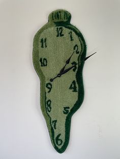 a green clock with numbers on the face is hanging from a wall in front of a white background