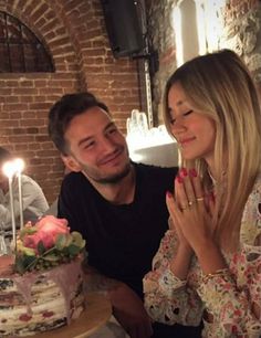 a man and woman sitting at a table with a cake in front of them that has candles on it