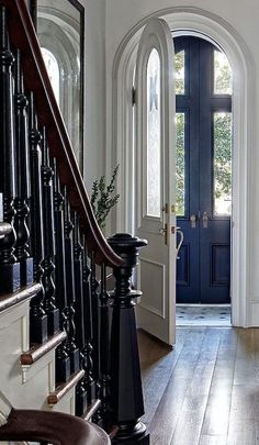 an entryway with a blue door and black railing, wooden floors, and white walls