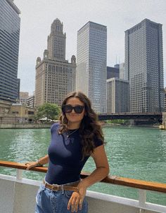 a woman standing on the side of a boat in front of tall buildings and water