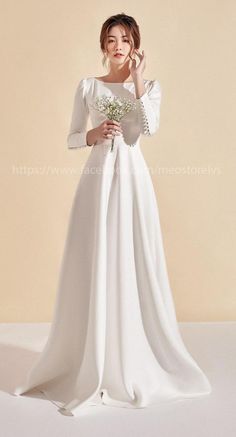 a woman in a white wedding dress holding a bouquet and posing for the camera with her hand on her face