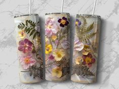 three tumbles with floral designs on them are shown against a marble background, one is empty and the other has two straws in it