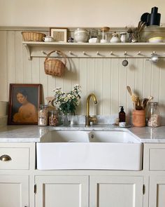 a white kitchen sink sitting under a window next to a shelf filled with pots and pans