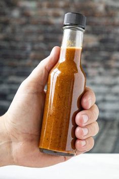 a hand holding a glass bottle filled with brown liquid