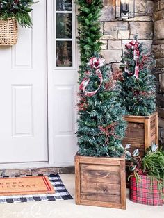 three christmas trees sitting in wooden boxes on the front porch next to a white door