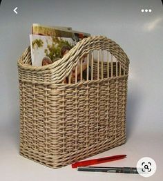 a wicker basket with magazines in it next to a pen and two pens on a white surface