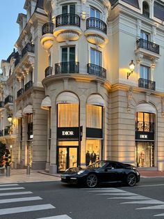 a black sports car is parked in front of a luxury store at dusk with its lights on