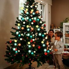 a young boy and woman standing in front of a christmas tree with lights on it