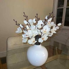 a white vase filled with flowers sitting on top of a glass tablecloth covered dining room table