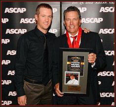 two men standing next to each other in front of a wall holding an award plaque