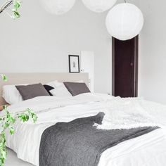 a bed with white sheets and pillows in a bedroom next to a plant on the wall