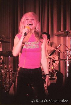 a woman singing into a microphone while standing in front of a drum set and other instruments