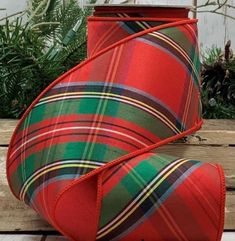 a red and green plaid lamp shade sitting on top of a wooden table next to greenery