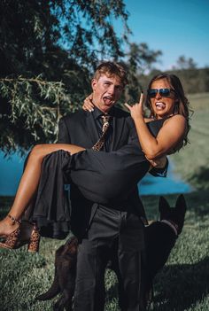 a man carrying a woman on his back in the grass next to a dog and tree