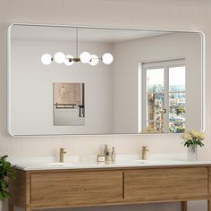 a bathroom vanity with two sinks and a large mirror above it, in front of a window