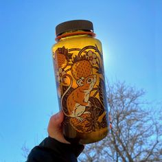 a hand holding up a yellow jar with an image of a squirrel on it and trees in the background