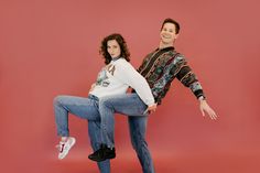 a man and woman are posing for a photo on a red background with their legs spread out