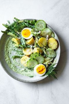 a white bowl filled with cucumber and boiled eggs on top of green sauce