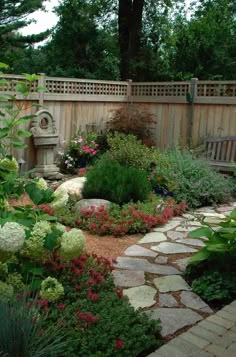 a garden with lots of flowers and plants around it, along with a wooden fence