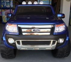 the front end of a blue truck parked in a garage with other cars behind it