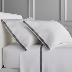 a bed with white sheets and grey trims in a hotel room or home setting