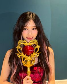 a woman in a red dress is holding a golden mask and posing for the camera