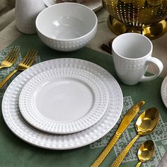 the table is set with white dishes and goldware