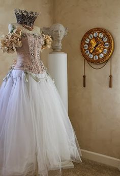 a white dress on display in front of a clock and wall with an ornate crown