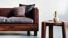 a couch and side table with a vase on it next to each other in front of a white wall