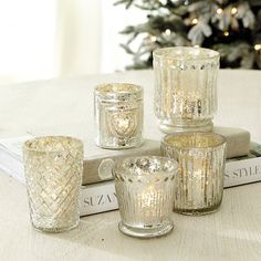 four glass votives sitting on top of a book next to a christmas tree