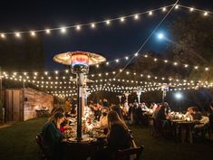 people are sitting at tables under lights in the dark outside with string lights strung over them