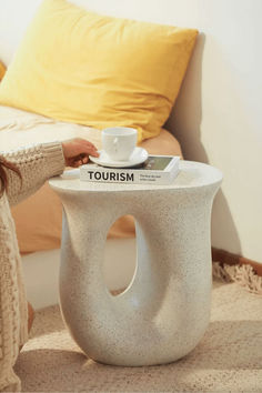 a woman sitting on the floor next to a table with a coffee cup on it