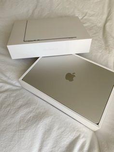 two apple laptops sitting on top of a white sheet covered bed with the box open