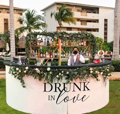 a man standing in front of a sign that says drink in love with flowers and greenery