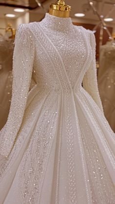 a white wedding dress with long sleeves and beading on display in a store window