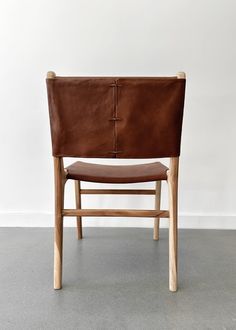 a brown leather chair sitting on top of a cement floor next to a white wall