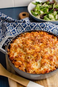 a casserole dish with cheese on top next to a bowl of salad and fork