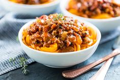 three bowls filled with pasta and meat on top of a table next to spoons