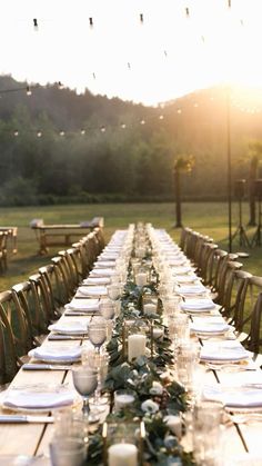 a long table is set with white plates and silverware for an outdoor dinner party