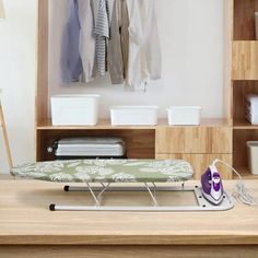 an ironing board sitting on top of a wooden table next to a shelf filled with clothes