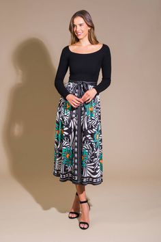 a woman standing in front of a wall wearing a black top and floral print skirt