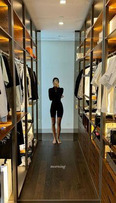 a woman standing in front of a closet filled with clothes and other clothing on shelves