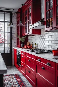 a kitchen with red cabinets and white tile backsplash, black countertops and an area rug