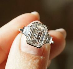 a woman's hand holding an emerald and diamond ring